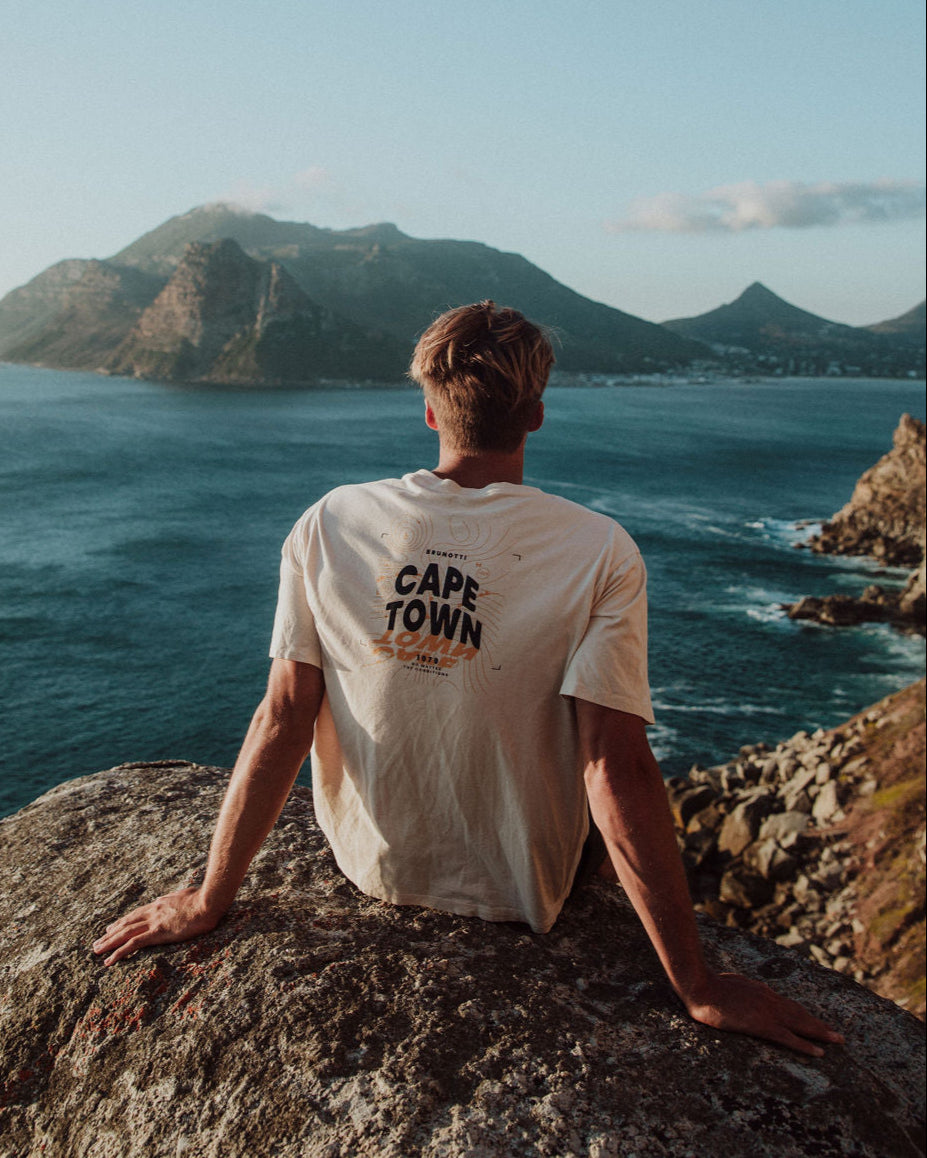 Person sitting on a cliff overlooking the ocean with mountains in the background