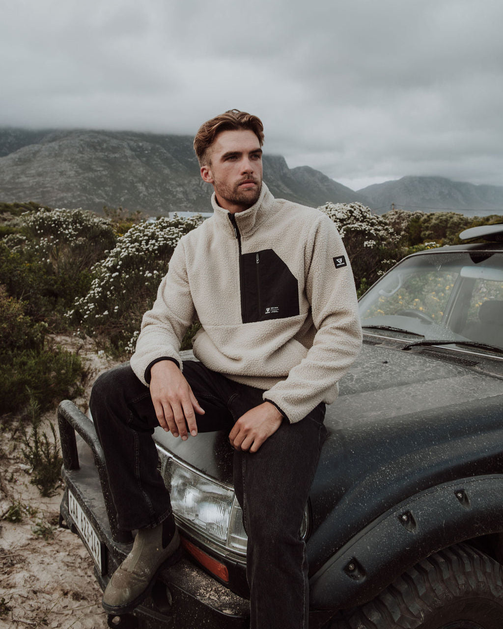 Man sitting on a car in a mountainous area with a cloudy sky