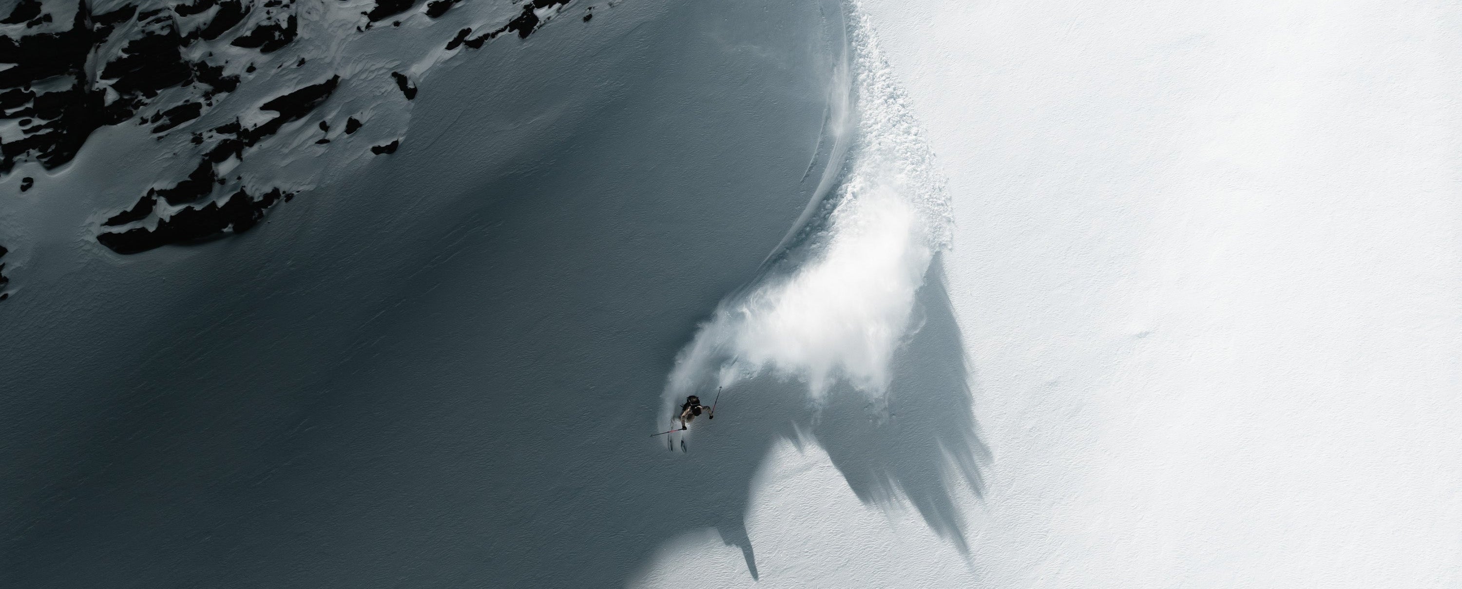 Person snowboarding down a snowy mountain with a large shadow cast by a nearby peak.