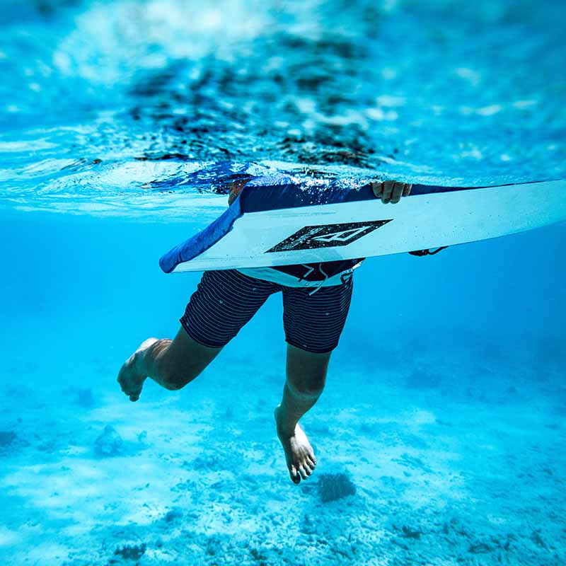 Underwater picture of a blue ocean with feet paddeling of a boy wearing a Brunotti Swim Trunk and riding a Brunotti Body Board